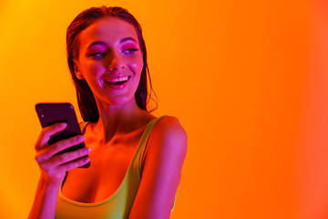 Image of brunette sensual woman wearing formfitting sportswear smiling while holding smartphone