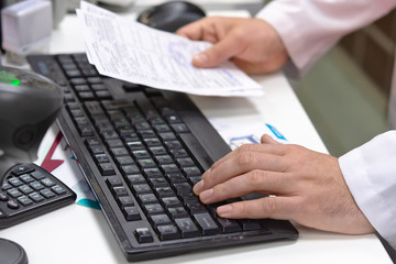Male medicine doctor hands hold recipe and type something on a laptop computer keyboard. Panacea and life saving. Pharmacist with a prescription in hand