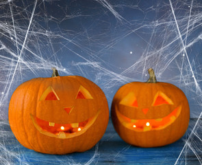 holidays, halloween and decoration concept - two pumpkins or jack o lanterns on table and spiderweb...