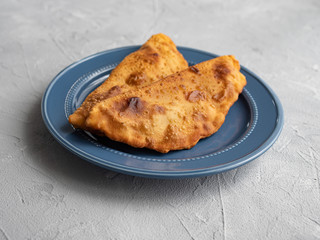Delicious fresh pasties stuffed with meat for the blue plate, grey concrete background.