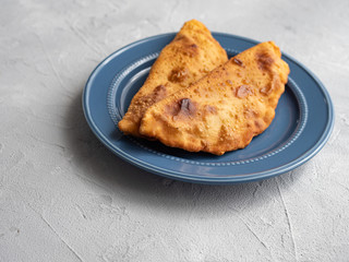 Delicious fresh pasties stuffed with meat for the blue plate, grey concrete background.