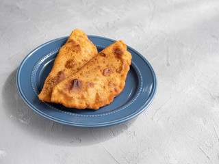 Delicious fresh pasties stuffed with meat for the blue plate, grey concrete background.