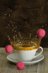 Cup of tea with splash and macarons on brown background