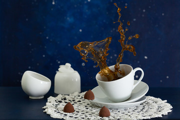 Double splash in a coffee cup with sugar bowl and chocolates on space background