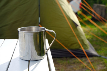 Fototapeta na wymiar camping metal mug on table with green tent in bcakground