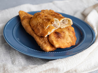Delicious fresh pasties stuffed with meat for the blue plate, grey concrete background.