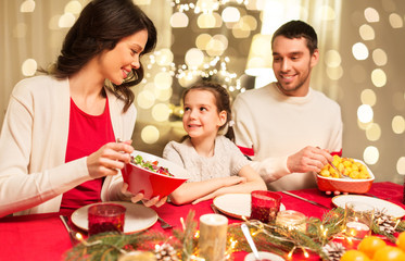 holidays, family and celebration concept - happy mother, father and little daughter having christmas dinner at home