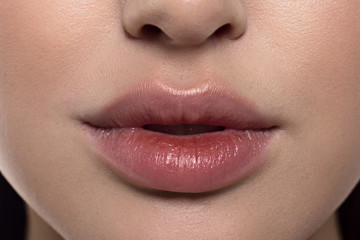 Fototapeta premium Cosmetics, makeup and trends. Bright lip gloss and lipstick on lips. Closeup of beautiful female mouth with natural lip makeup. Beautiful part of female face. Perfect clean skin in red light