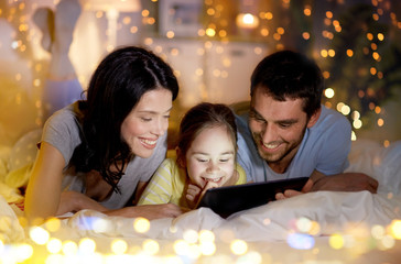 people and family concept - happy mother, father and little daughter with tablet pc computer in bed at night at home