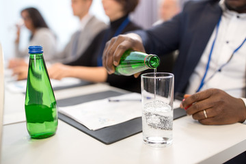 business and people concept - close up of african american businessman pouring water from bottle to glass at international conference