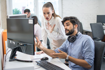 Surprised young business woman and handsome young businessman looking at computer screen in office.