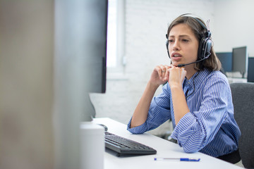Beautiful young call centre telephone worker talking with a client while sitting bellow computer. Copy space on left side.