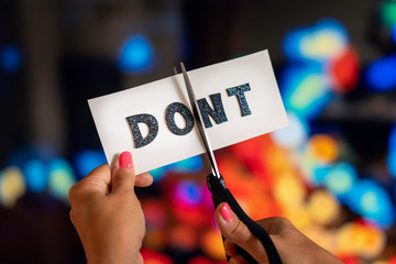 Woman hand are cutting over a sign with scissors converting the word dont to do. Blurry city light...