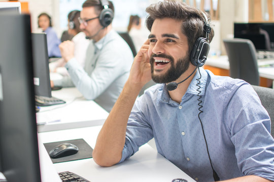 Friendly happy handsome young man with hands-free headset using computer in a call centre