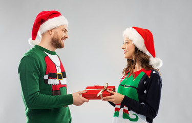 people and holidays concept - happy couple in santa hats with christmas gift at ugly sweater party