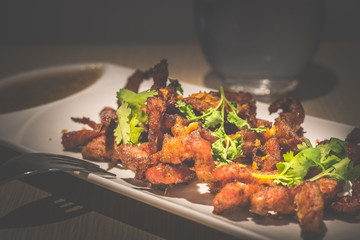 Deep fried thai pork neck served with parsley and garlic dipping sauce on a white porcelain plate