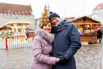 love, winter holidays and people concept - happy senior couple hugging at christmas market on town hall square in tallinn, estonia