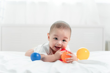 Portrait of a crawling baby on the bed in her room and playing ball toy, Adorable baby boy in white sunny bedroom. Newborn child relaxing in bed. Nursery for young children.