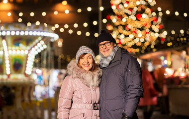 Obraz premium love, winter holidays and people concept - happy senior couple hugging at christmas market on town hall square in tallinn, estonia