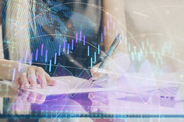 A woman hands writing information about stock market in notepad. Forex chart holograms in front. Concept of research. Double exposure