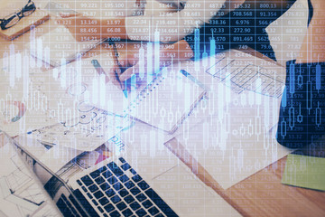 A woman hands writing information about stock market in notepad. Forex chart holograms in front. Concept of research. Double exposure