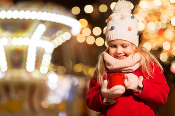holidays, childhood and people concept - happy little girl with cup of tea at christmas market in...
