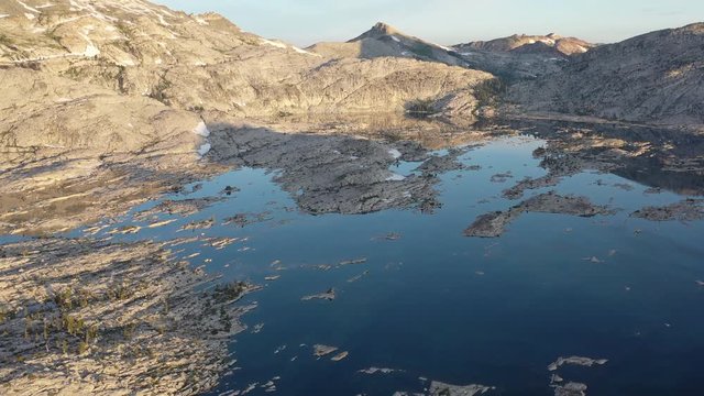An aerial view shows early morning light illuminating a rocky alpine lake in the Sierra Nevada mountains. These California mountains are made up of 100 million year old granite sculpted by glaciers.