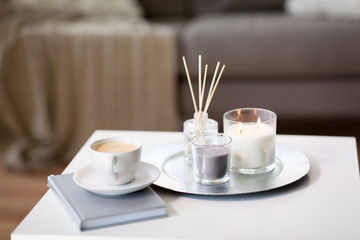 hygge and aromatherapy concept - coffee, candles, book and aroma reed diffuser on table at home