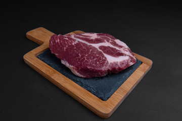 Closeup of a piece of raw meat on a cutting board. Black background. 