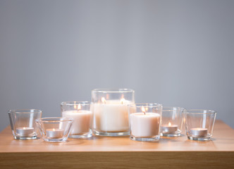 decoration, hygge and cosiness concept - burning white fragrance candles on wooden table