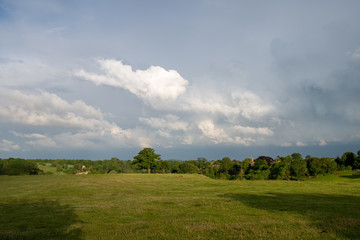 Obraz premium Storm clouds building over green fields and trees on a summer day in the countryside near Shenington, Oxfordshire