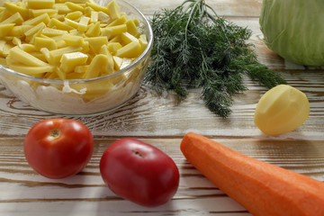 The closeup potatoes cut into long slices are placed in a glass transparent baking dish. The process of cooking the Orlov-style meat. Lying next to the whole clean vegetables. Vintage wooden backgroun