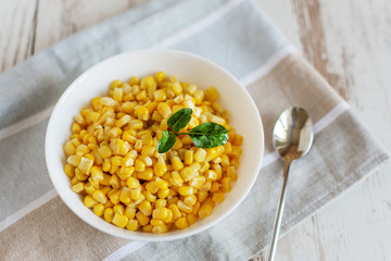 Canned sweet corn in a white bowl on napkin wooden table background.