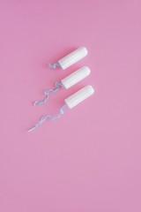 Three hygienic tampons on a pink background. Menstrual mothly cycle, means of protection. Top view, flat lay, copy space for text.