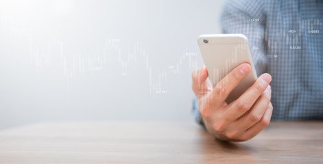 close up expert investor of  stock trader hand holding smartphone and monitoring trading board for forecasting about buying or selling currency exchange rate , business with technology concept