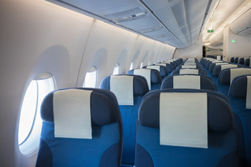An economy class clean cabin of the airplane - empty blue chairs - opened portholes