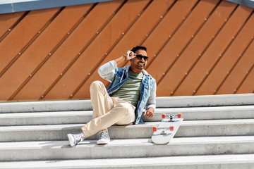 people and leisure concept - smiling indian man with skateboard sitting on stairs in city