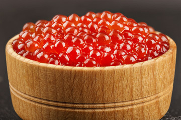 red caviar in a wooden bowl on a black background for designers