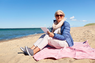 people and leisure concept - happy senior woman writing to notebook on summer beach in estonia