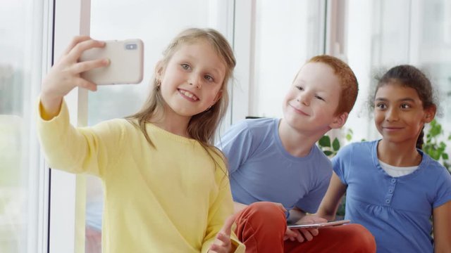 Handheld shot of cute little schoolchildren taking selfie on mobile phone during break