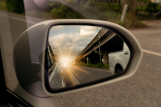 Abstract Blurred image. The view of the side of the mirror white car. with the car from behind with the bright orange light and Bridge.