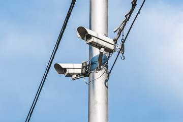 a pair of surveillance cameras on a metal pole against a blue sky