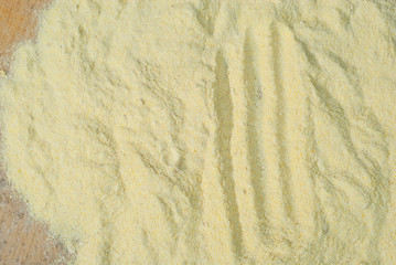 Texture of corn flour on a wooden table. Yellow flour closeup on old plywood board. Traces from the toes of the croup.