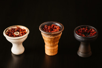  different types of cups with tobacco for hookahs. silicone and clay. on a black background with tobacco inside.