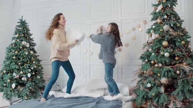 Smiling mother and daughter playing with pillows in luxury bedroom.