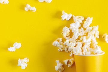 Paper cup with popcorn on yellow background. Flat lay, top view, copy space