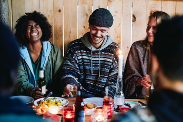 Smiling friends holding drinks and talking in log cabin