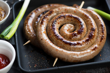 Closeup of barbecued coiled sausages in a cast-iron tray, selective focus, studio shot