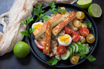 Metal tray with quinoa, fried cheese, tomatoes, cucumber and eggs, studio shot
