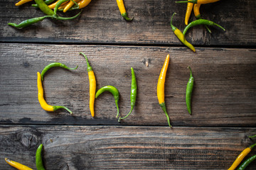 Word CHILI made of raw organic yellow and green chili cayenne peppers on old wooden table